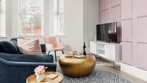 Moderni olohuone, jossa on tummansininen sohva, pyöreä kultainen sohvapöytä ja litteänäyttöinen televisio valkoisessa kaapissa.