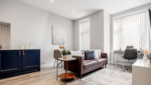A modern living room with a dark blue cabinet, a brown leather sofa, a coffee table, and a desk with a chair. - Modern & Mellow 1-bed Apt w/ Free Parking & Wi-Fi (Bournemouth)