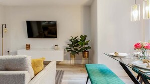 Una sala de estar moderna con un sofá, una mesa de comedor dispuesta con platos y flores, y un televisor de pantalla plana montado en la pared.