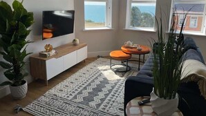 A living room with a TV, a sofa, a coffee table, and a view of the sea.