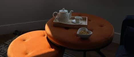 Ein Zimmer mit Meerblick, ein kleiner runder Tisch mit Teekanne und Tasse sowie ein orangefarbener Hocker.