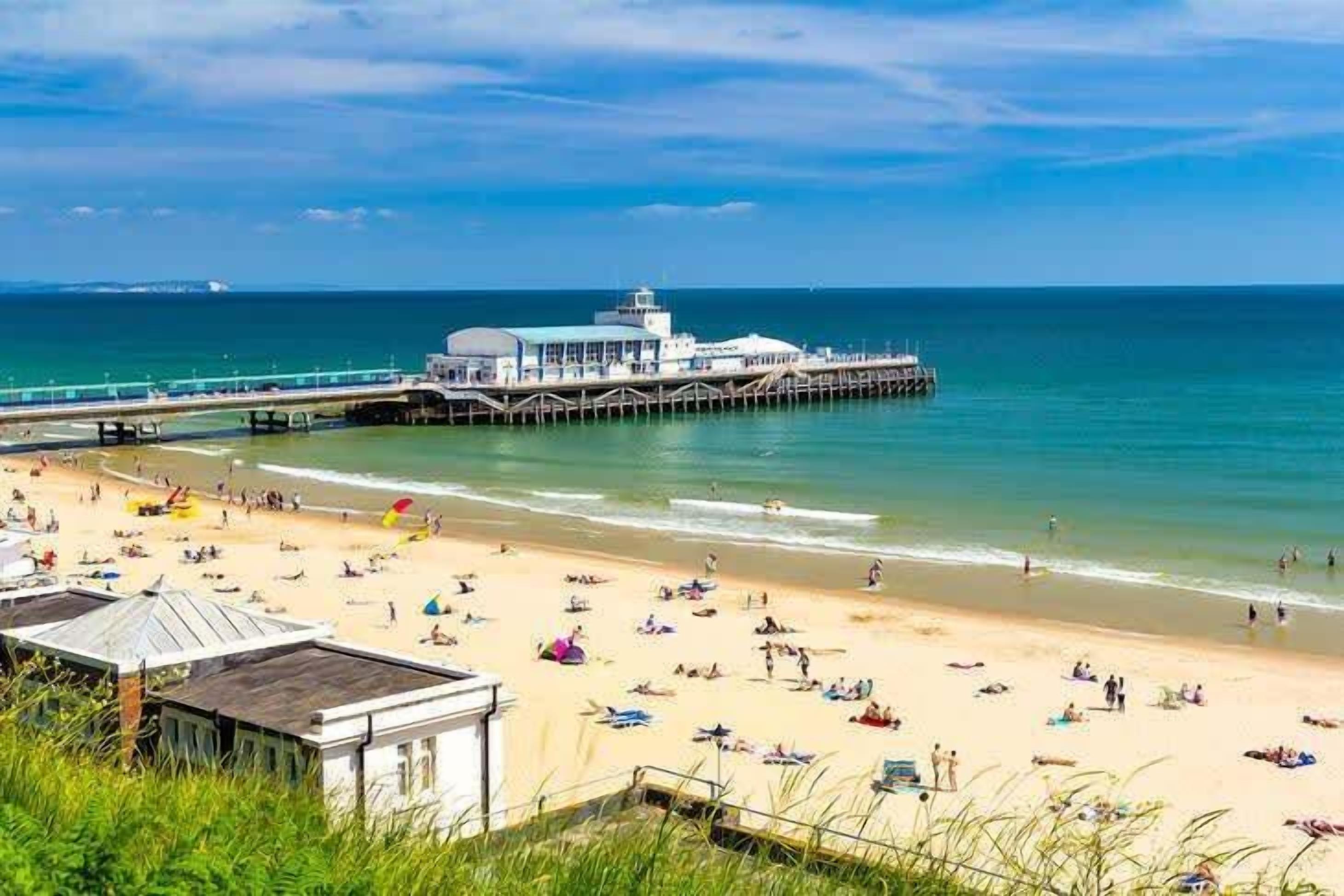 A beach with a pier extending into the sea, featuring a building with a dome-like structure.