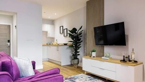 Una sala de estar moderna con un sofá púrpura, un televisor de pantalla plana montado en un panel de madera y una planta en maceta.