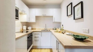 Una cocina moderna con armarios blancos, encimera de madera y un lavamanos. Hay cuadros enmarcados en la pared y un bol verde sobre la encimera.