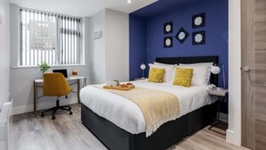 A modern bedroom with a large bed, a desk, and a window with blinds. - Comfy & Cosy 1-bed Apt w/ Free Parking & WiFi (Bournemouth)