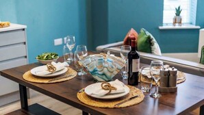 Une table à manger dressée avec des assiettes, des couverts, des verres et une bouteille de vin, ainsi qu’un bol et un objet décoratif placés sur la table.