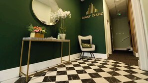 A reception area with a checkered floor, a round mirror, a console table with decorative items, a chair, and a wall sign reading "tower house". - Spacious Seaside 2-Bed Apt w/ Free Gym & Parking (Bournemouth)