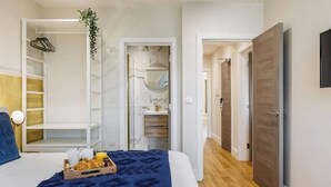 Ein Schlafzimmer mit Bett, Nachttisch mit Frühstücksgebäck, Kleiderschrank, Spiegel und einer Tür zu einem weiteren Raum.