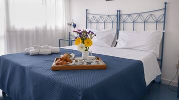 Un lit bien fait, avec une tête de lit bleue, un plateau de croissants, un vase de fleurs et une table de chevet avec une lampe.