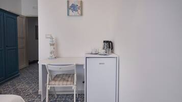 A small room with a white desk, a chair, a small white refrigerator, and a blue cabinet.