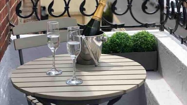 En balkon med et bord, to vinglas og en champagneflaske i et spand.