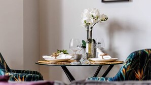 A dining area with a table set for two, framed botanical prints on the wall, and a decorative vase with white flowers.