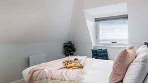 Un dormitorio con cama, ventana, planta y una bandeja con cosas para el desayuno.