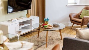 A modern living room with a glass coffee table, a leather armchair, a flat-screen TV, and a bookshelf. - Stunning & Spacious 1-Bed Apt w/ Free Gym & PKG (Bournemouth)