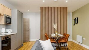 A modern kitchen with a microwave, oven, and coffee maker. There is a dining area with a table and chairs, and a sofa in the foreground. - Stunning & Spacious 1-Bed Apt w/ Free Gym & PKG (Bournemouth)