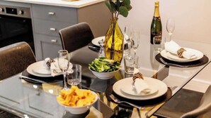 A dining table set for four with plates, glasses, a vase with greenery, and a bottle of champagne. - Spacious Garden, 2-Bed Apt w/ Free Gym & Parking (Bournemouth)