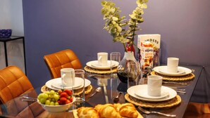 A dining table set with white plates, cups, and a glass pitcher, accompanied by a bowl of fruit and croissants.