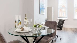 A modern dining area with a glass table, two chairs, and a dining set. - Comfy Seaside Studio Apt w/ Free Gym & Wi-Fi (Bournemouth)