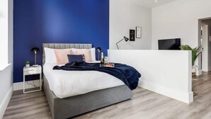 A modern bedroom with a grey bed, white walls, and a blue accent wall. - Comfy Seaside Studio Apt w/ Free Gym & Wi-Fi (Bournemouth)