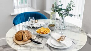 Een eettafel met een marmeren blad, een schaal met chips, een brood en een fles witte wijn.