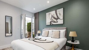 Een moderne slaapkamer met een groot bed, een nachtkastje met een lamp, een lijst met abstract schilderij aan de muur en uitzicht op het landschap door een schuifdeur.