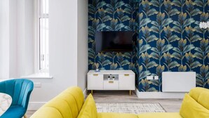 Een moderne woonkamer met een grote flatscreen televisie aan de muur, een witte salontafel en een gele bank.