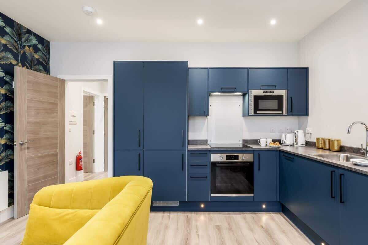 Una cocina moderna con armarios azules, microondas, horno y una silla amarilla.