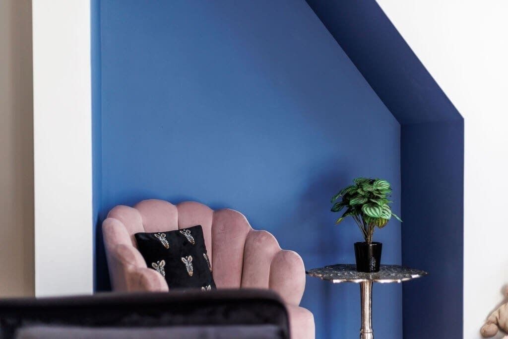 A room with a pink chair, a small round table with a potted plant, and a blue accent wall.