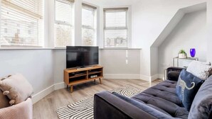 Un salon moderne avec un grand téléviseur à écran plat, un canapé foncé et un tapis à motifs.