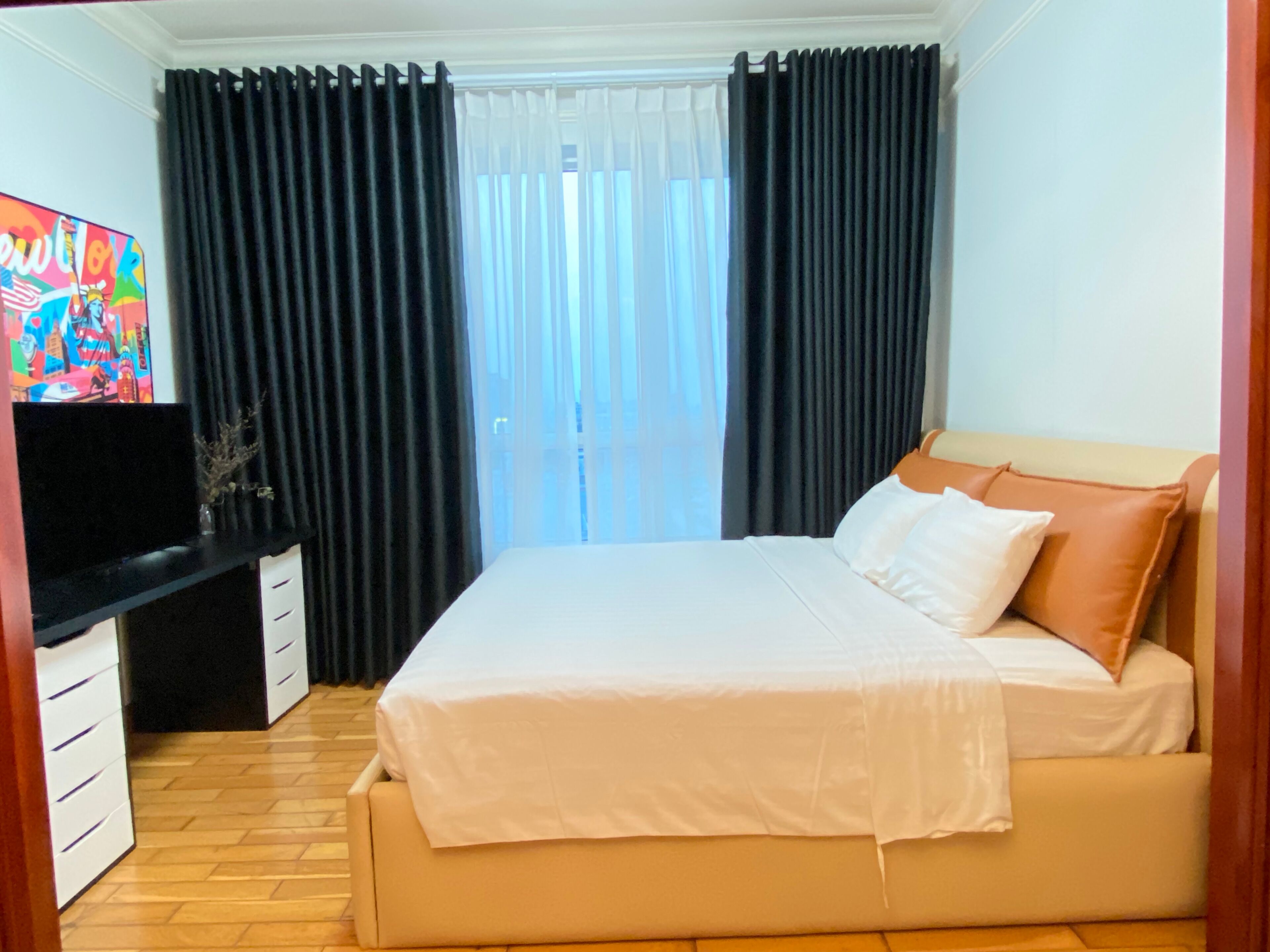 A bedroom with a bed, a TV on a stand, and a window with curtains.