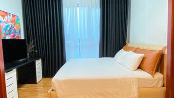 A bedroom with a bed, a TV on a stand, and a window with curtains.