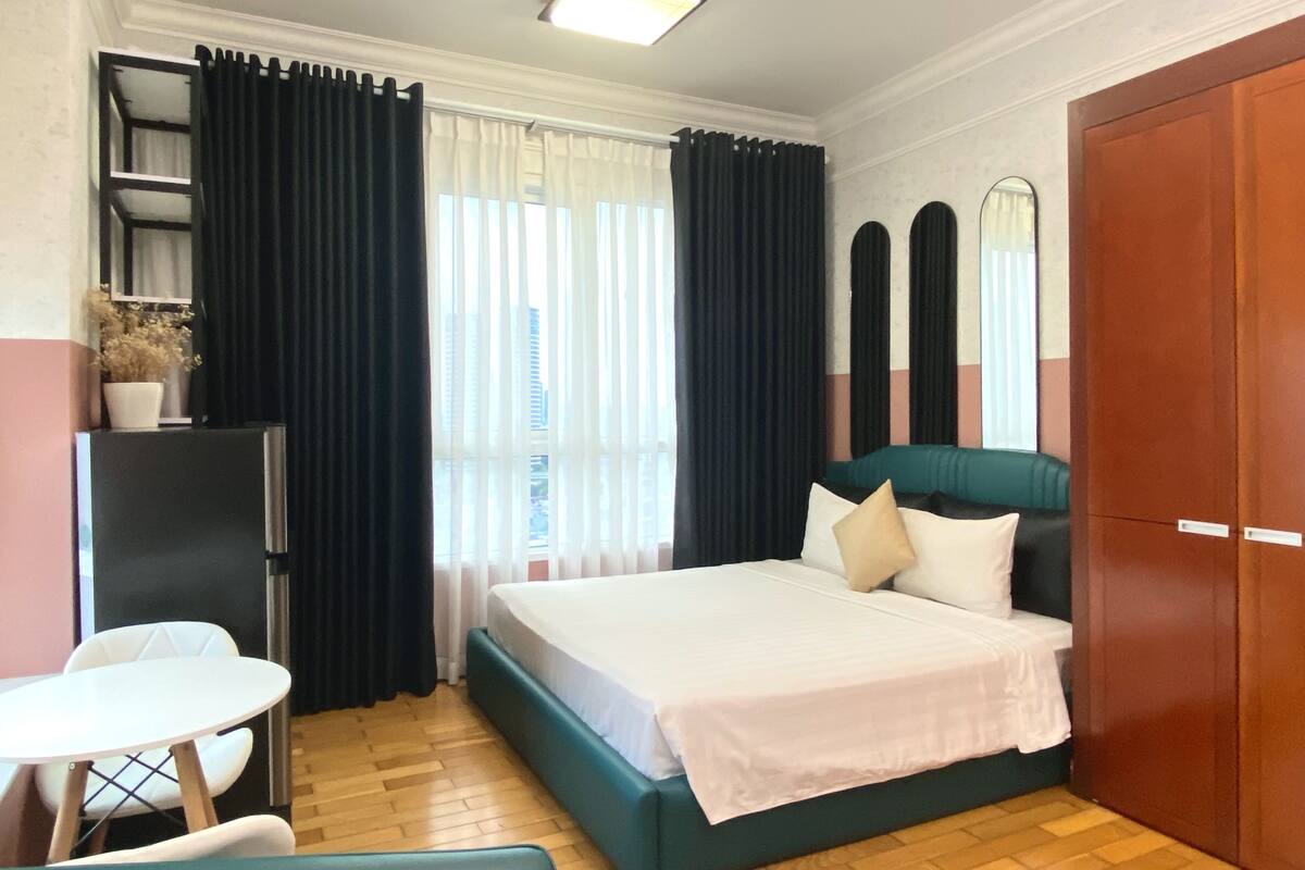 A hotel room with a bed, a desk, a chair, a wardrobe, and a window with curtains.