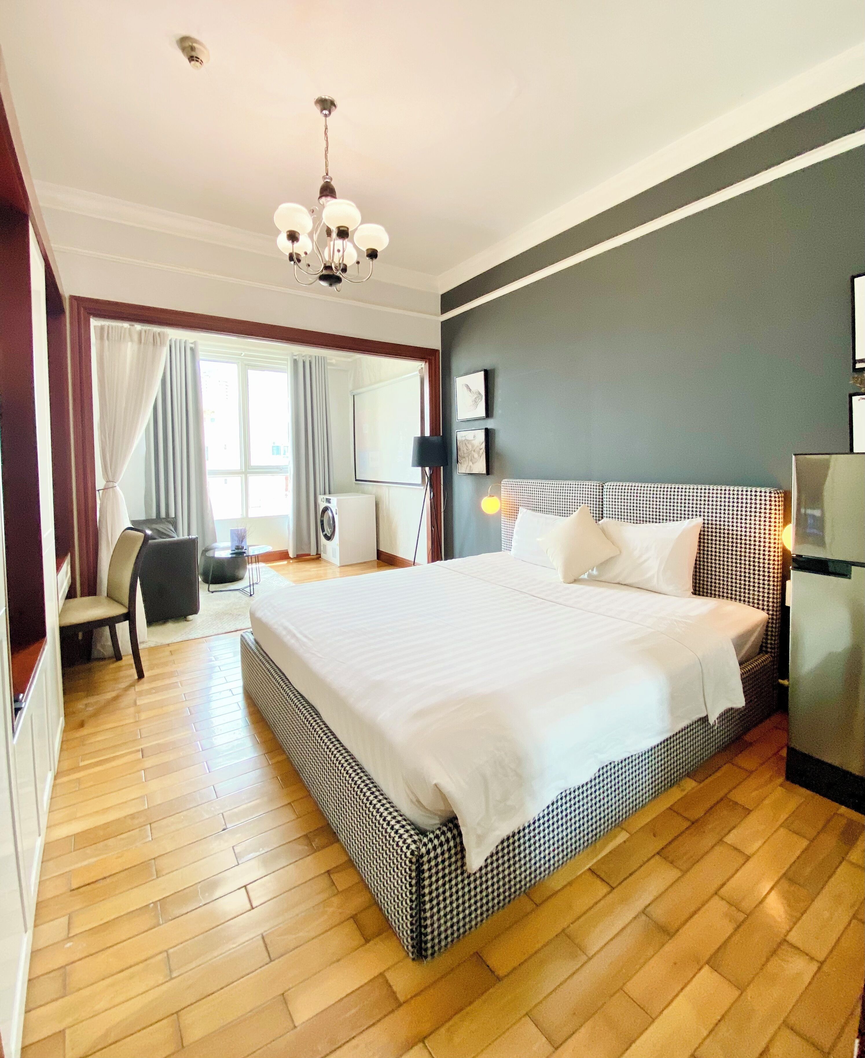 A hotel room with a large bed, a desk, a chair, a washing machine, and a refrigerator.