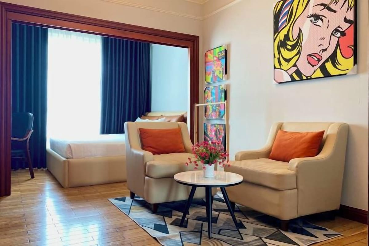 A hotel room with a sofa, armchairs, a small table with flowers, and artwork on the wall.