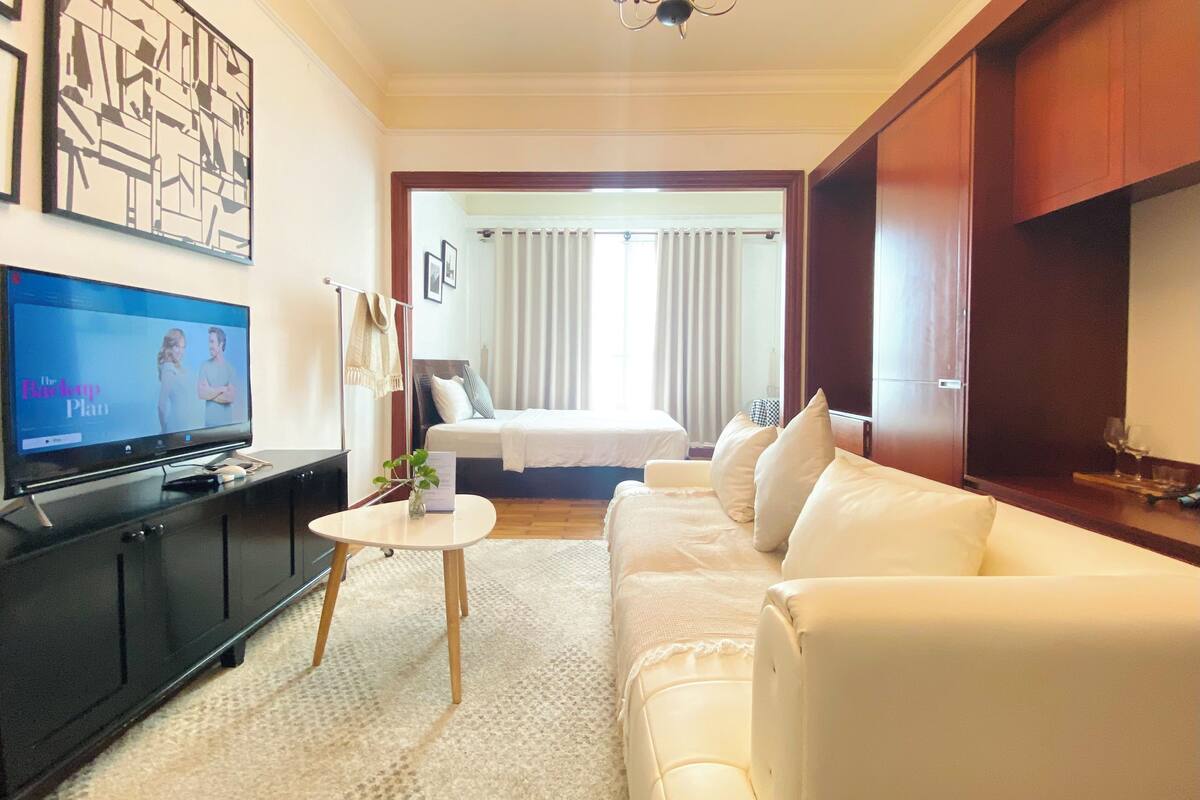 A hotel room with a TV, a sofa, a bed, and a chandelier.