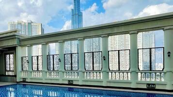 A swimming pool with a tiled edge, large windows with decorative ironwork, and a view of a tall skyscraper in the background.