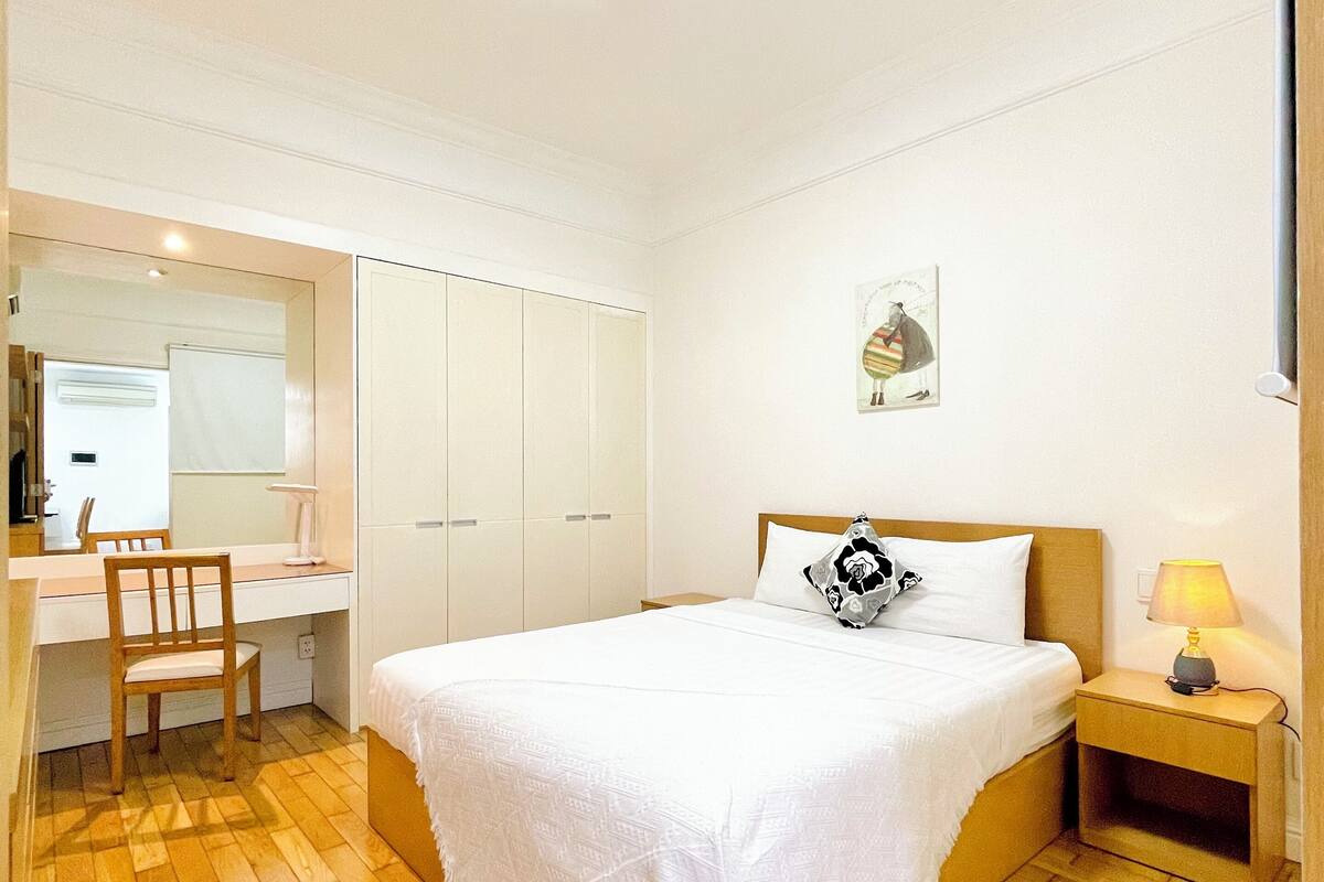 A bedroom with a bed, bedside table, lamp, chair, desk, and wardrobe.