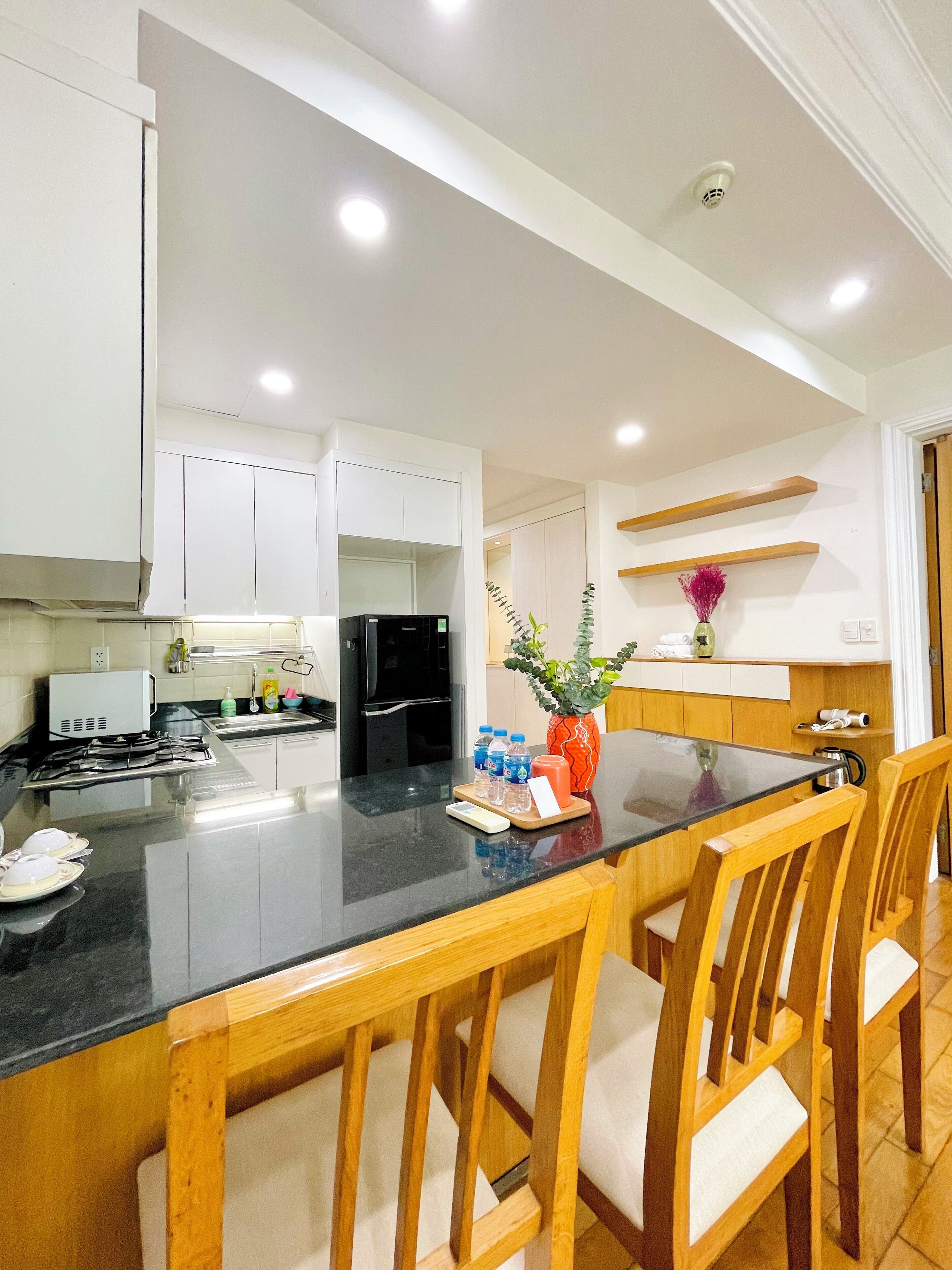 A modern kitchen with white cabinets, a black countertop, and wooden chairs.