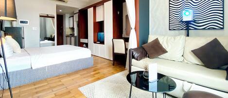 A modern hotel room with a bed, a sofa, a coffee table, and a TV.