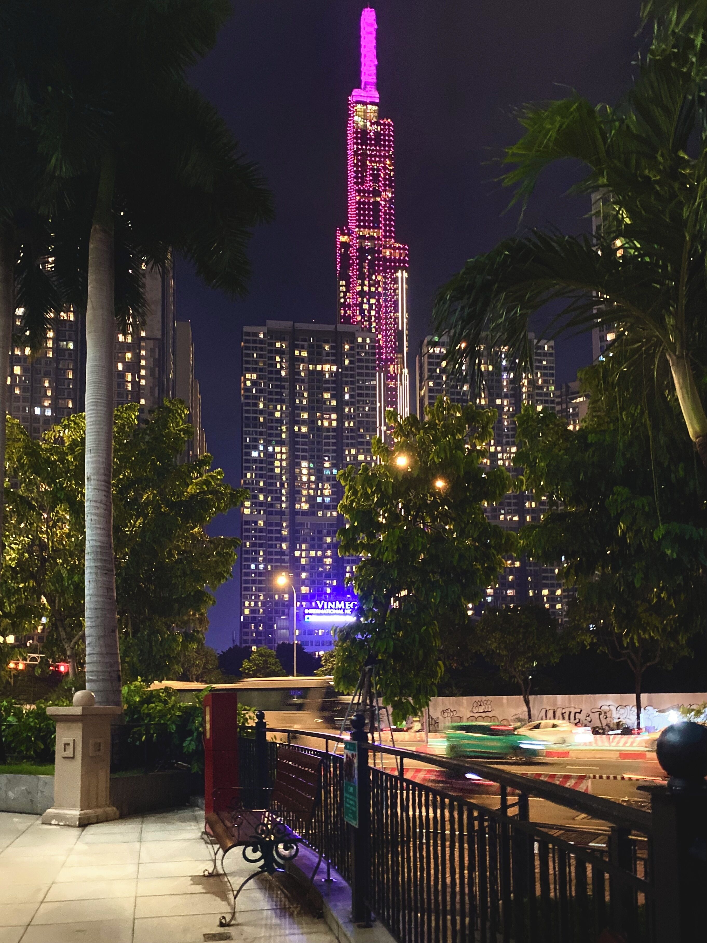 A night view of a cityscape with a prominent building lit in pink and blue.