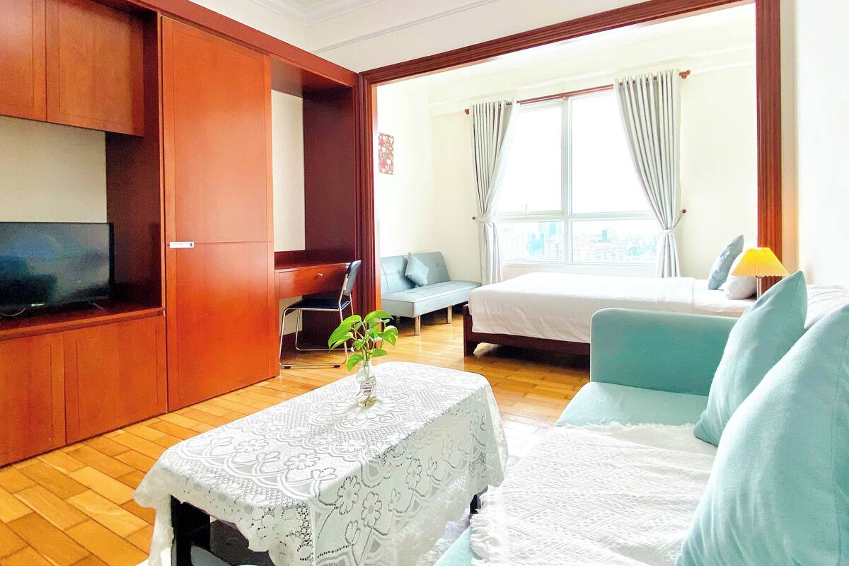 A hotel room with a bed, a sofa, a TV, a desk, and a window with curtains.