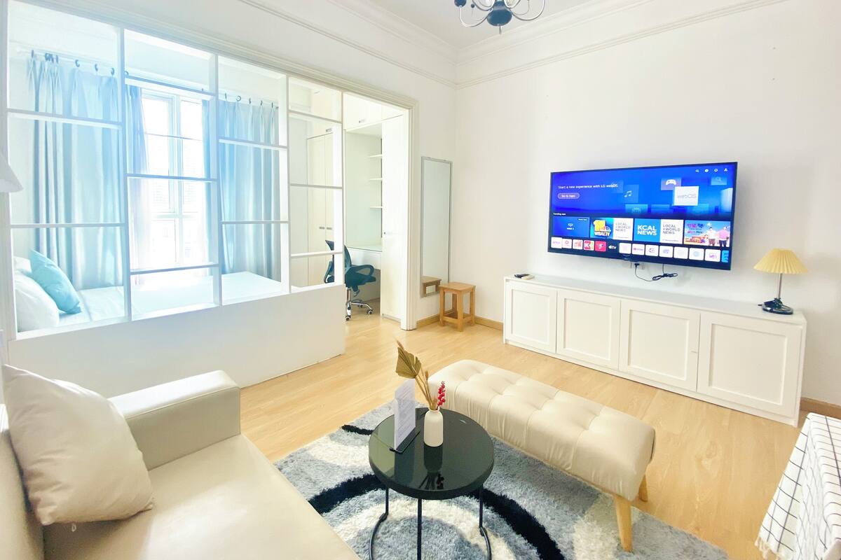 A modern living room with a large window, a flat-screen TV, a sofa, a coffee table, and a TV stand.