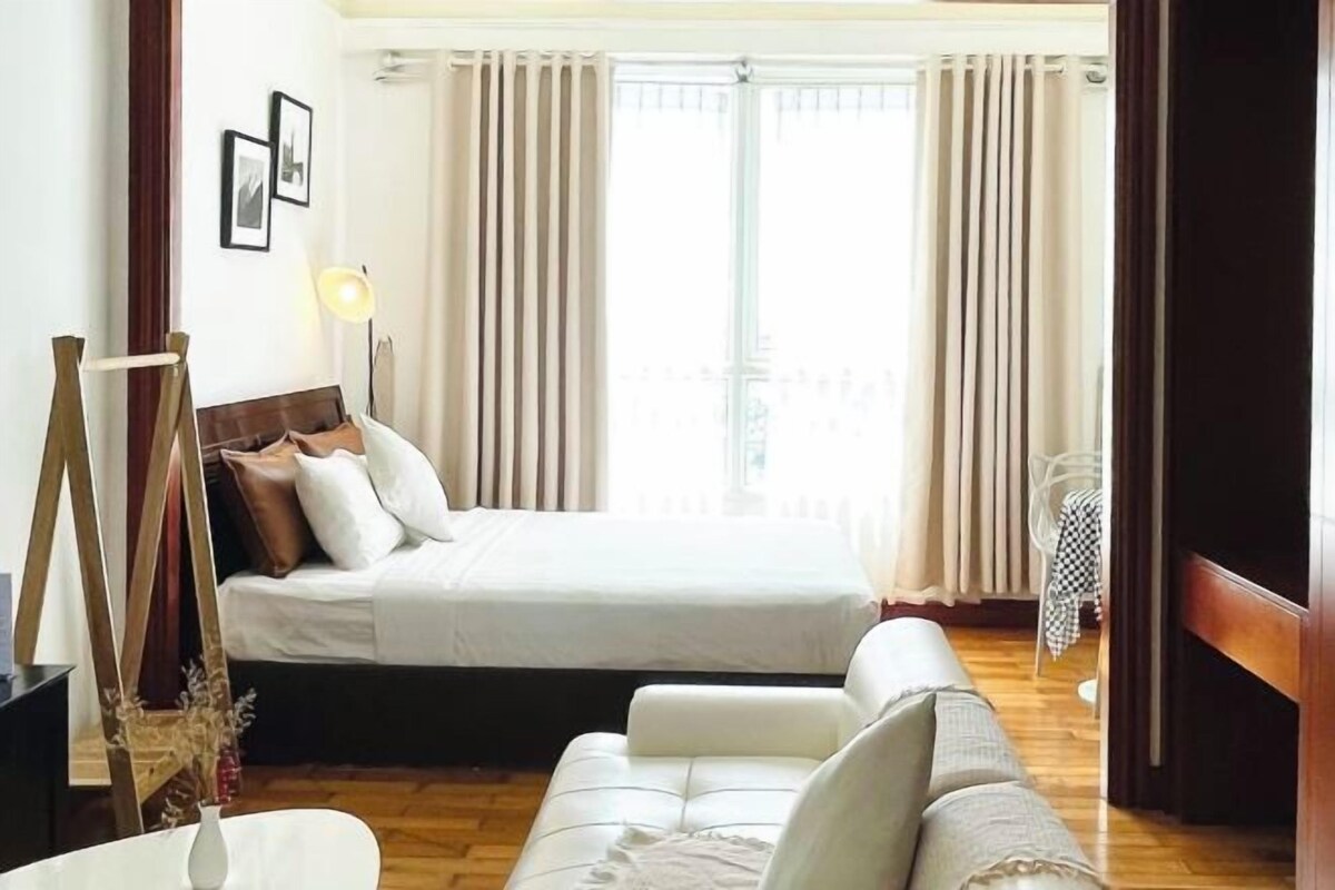 A bedroom with a bed, a sofa, a bedside table, and a window with curtains.