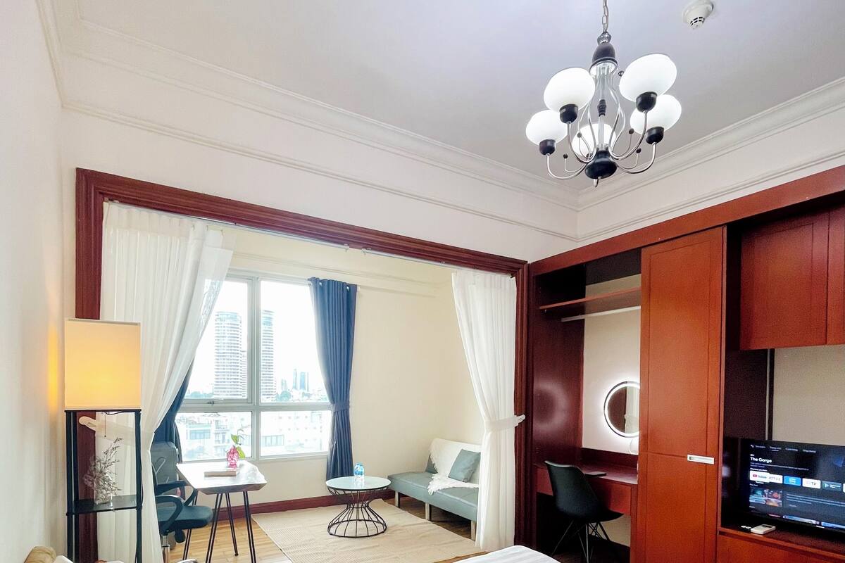 A hotel room with a large bed, a desk, a chair, a TV, and a view of the city.