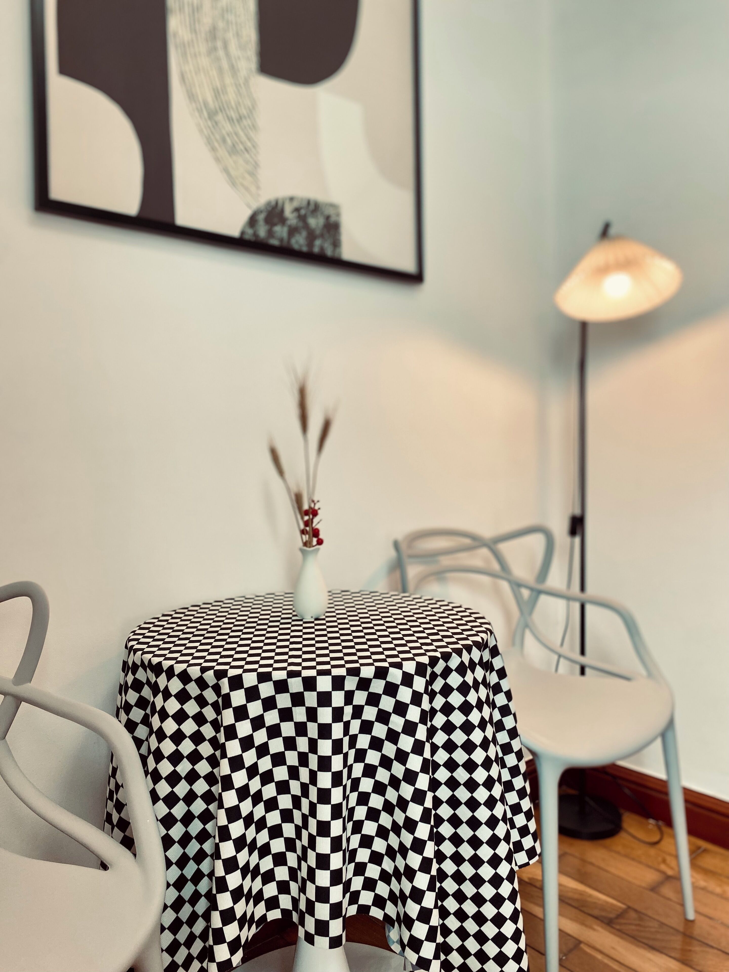 A dining area with a checkered tablecloth, a vase with dried flowers, and a modern lamp.