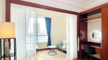 Una habitación de hotel con una cama, un espejo redondo, una mesita, una silla, un sofá y vistas de la ciudad a través de la ventana.