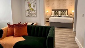 A modern hotel room with a green sofa, a large bed with a wooden headboard, and a wall-mounted artwork of birds. - Spacious 1-bed Studio Apt w/ Free Parking & WiFi (Bournemouth)