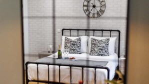 A neatly made bed with a metal frame, white bedding, and patterned pillows. A clock is mounted on the wall above the bed. - NEW! Superb Studio Apt w/ Free Parking & WiFi (Bournemouth)