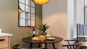 A dining area with a round table, two chairs, a wine bottle, glasses, a bowl of fruit, and a potted plant. - NEW! Superb Studio Apt w/ Free Parking & WiFi (Bournemouth)