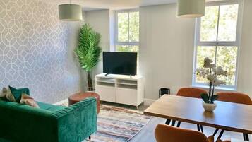 Un salon moderne avec un canapé vert, un téléviseur à écran plat, une table à manger avec des chaises et une grande fenêtre.